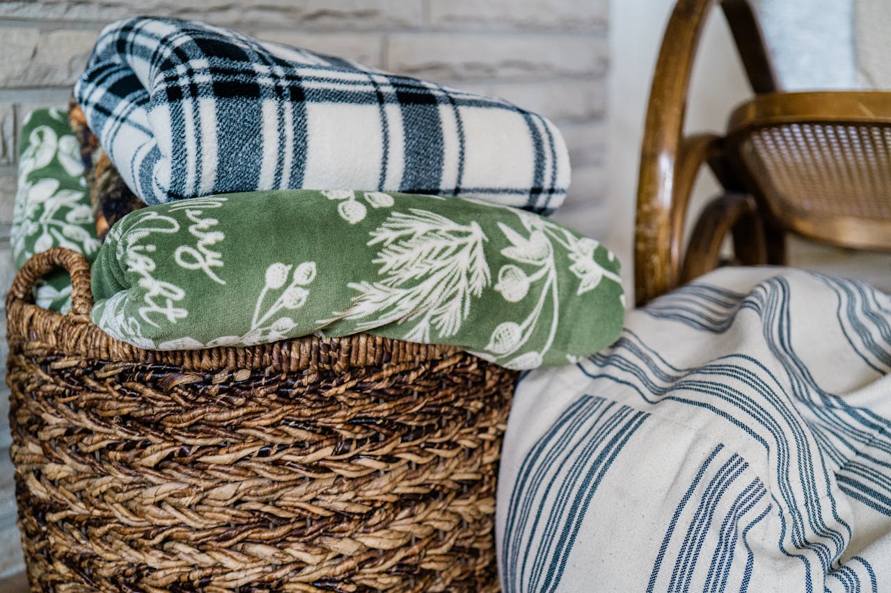 A wicker basket filled with various soft blankets and textiles, perfect for home comfort.